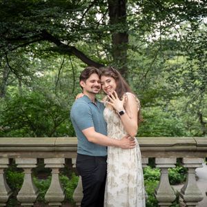 Happy newly engaged couple embracing and showing off engagement ring at Central Park balustrade.
