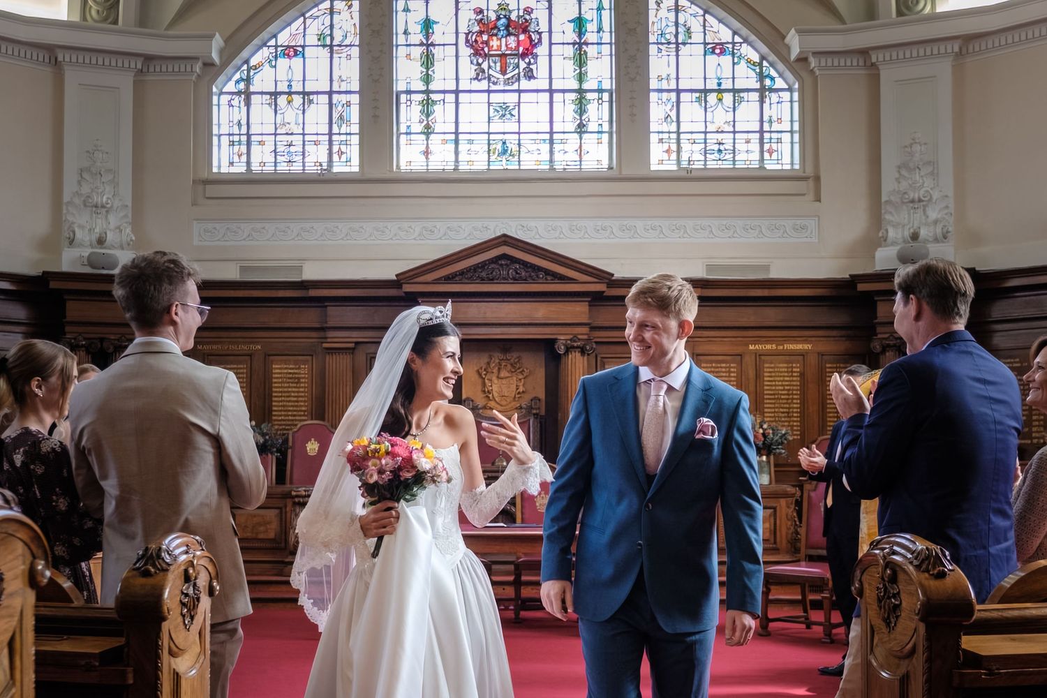 A bride and groom stand at the altar in a church, surrounded by their wedding party.