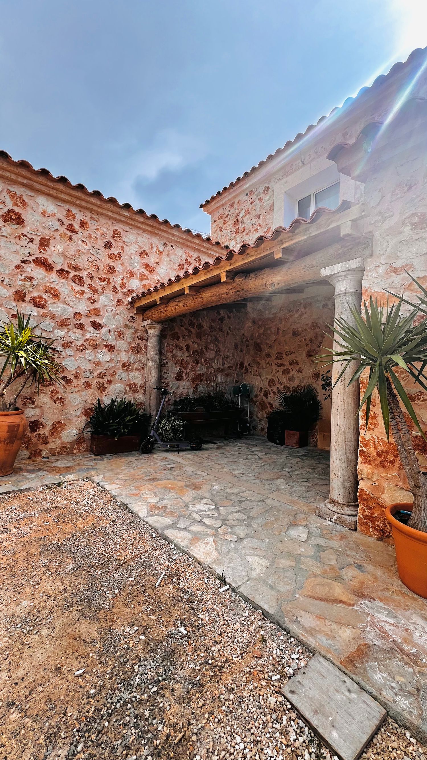 A stone-walled courtyard with a tiled floor, potted plants, and a decorative column supporting the roof.