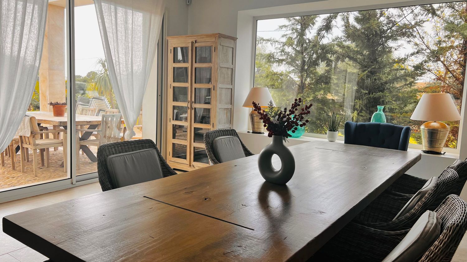 A spacious and modern dining room with a large wooden table, black chairs, and a decorative vase on the table.