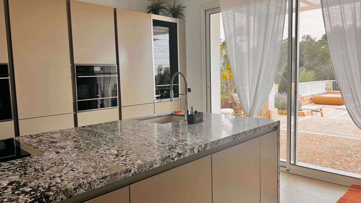 A modern kitchen with granite countertops, wood cabinets, and a large window overlooking a scenic outdoor view.