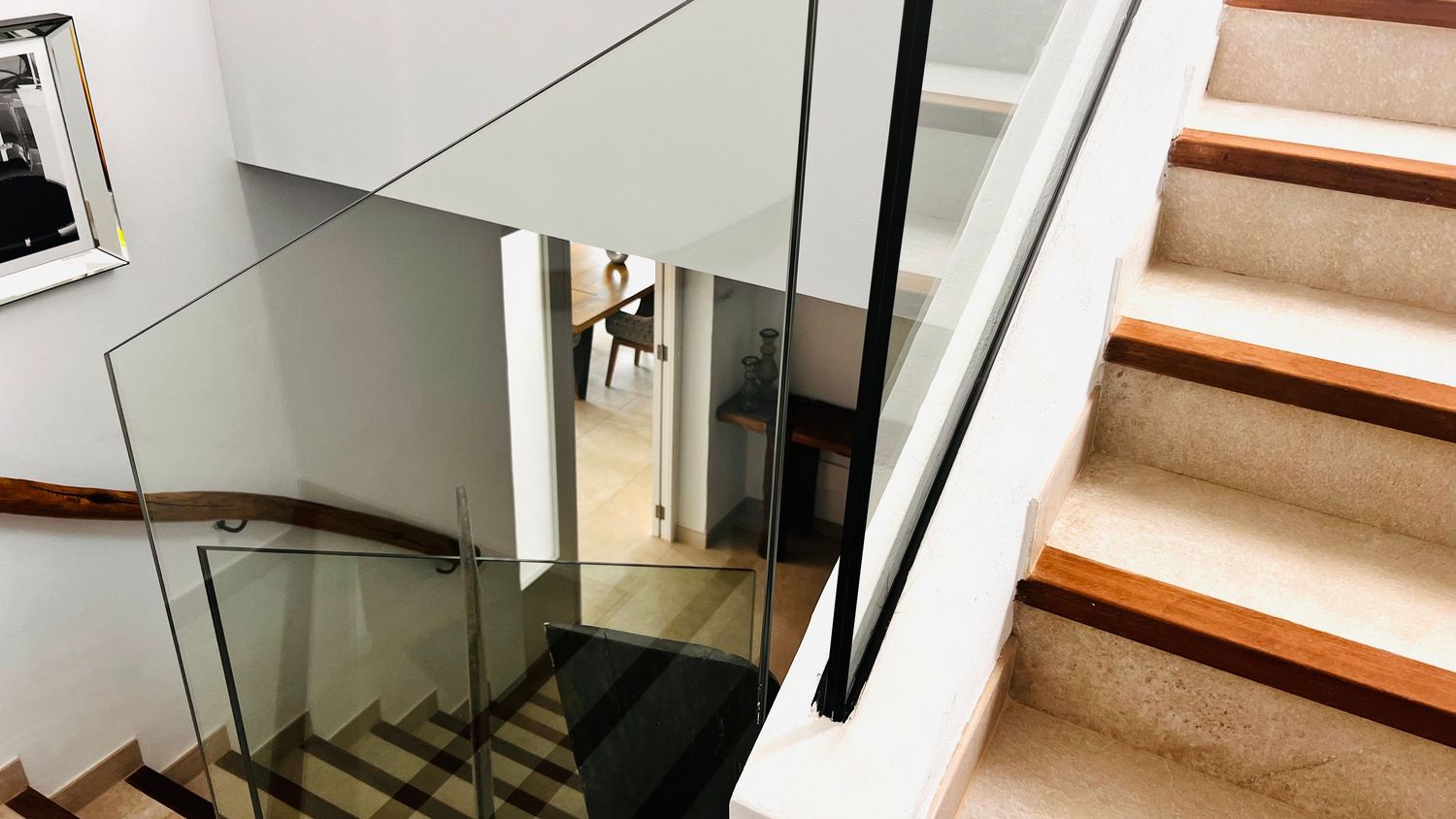 A staircase with wooden steps leading up, next to a glass door and white walls.