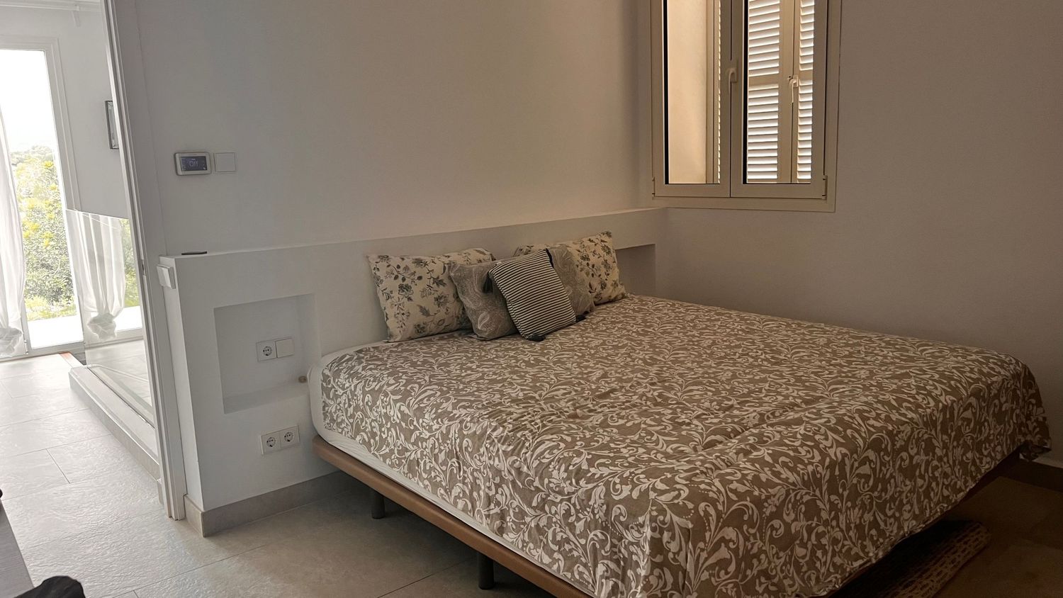 A cozy bedroom with a patterned comforter on the bed and a window providing natural light.