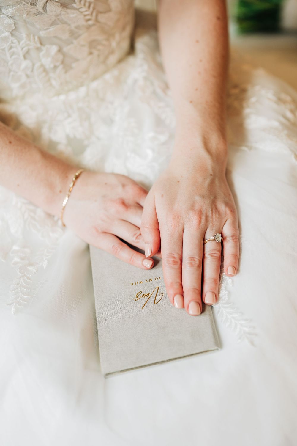 A delicate silver ring sparkles against white lace fabric as hands gently hold a light gray wedding vow book.