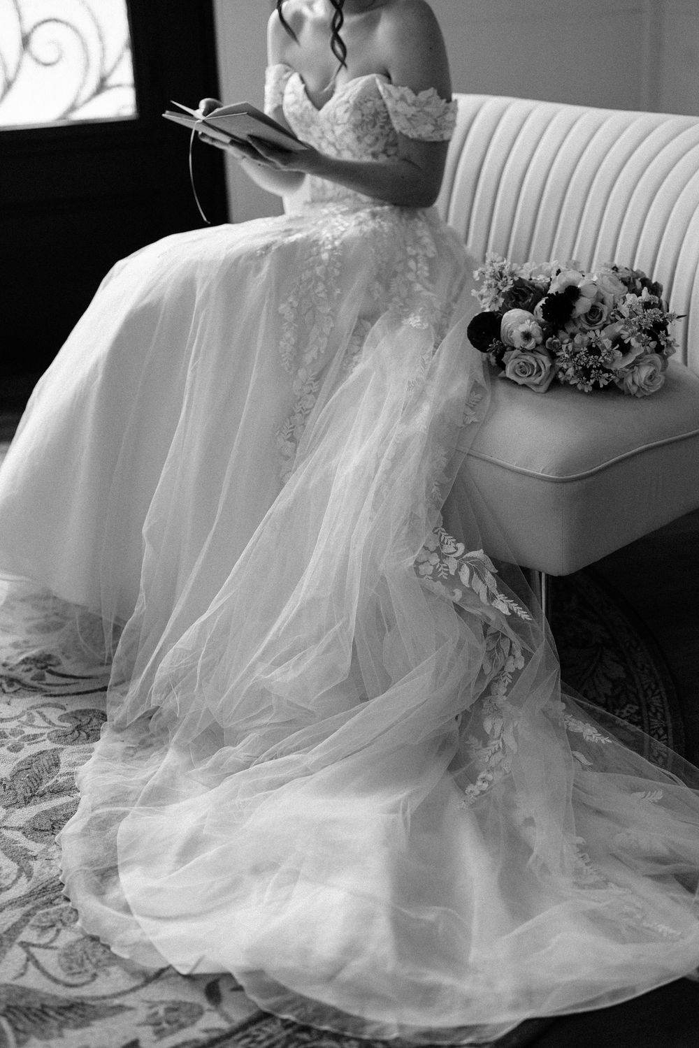 Flowing white wedding dress with delicate tulle layers draped elegantly over a chair in black and white photography.
