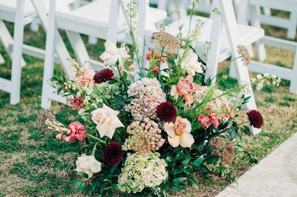 Elegant wedding ceremony aisle decorated with lush pink and burgundy floral arrangements along white chairs.