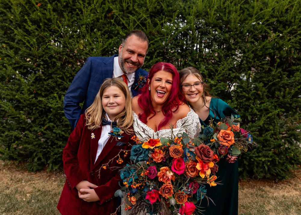 Happy family poses together at a wedding, bride with red hair holds colorful bouquet of orange and teal flowers at Founders One Nine