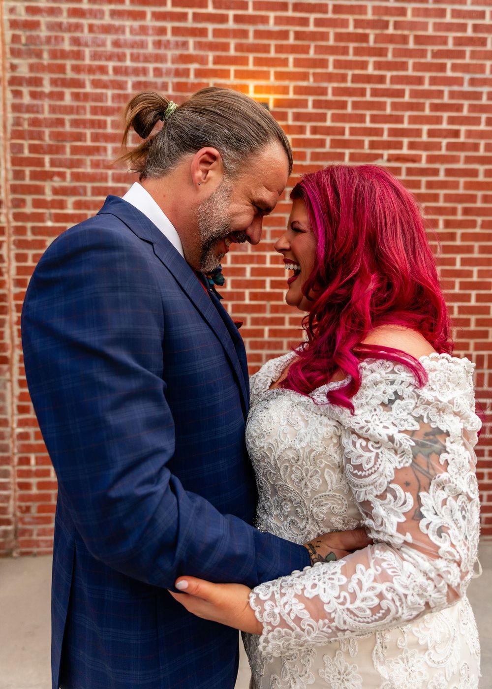 Bride with vibrant red hair in lace gown and groom in navy suit share a tender moment at their wedding at Founders One Nine in Omaha, NE.