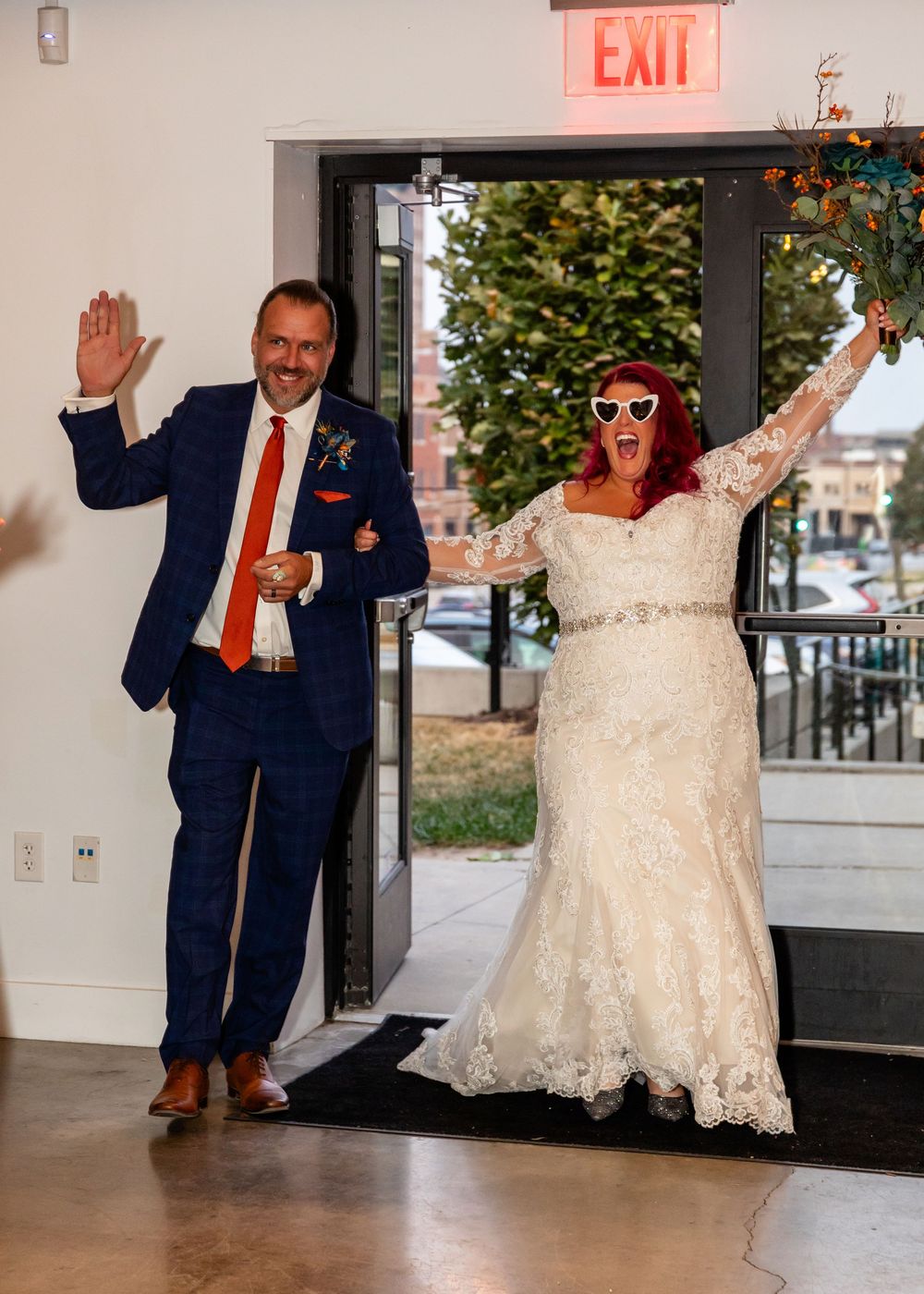 Joyful bride in lace gown with red hair and groom in navy suit making grand entrance at wedding reception at Founders One Nine in Omaha, NE.