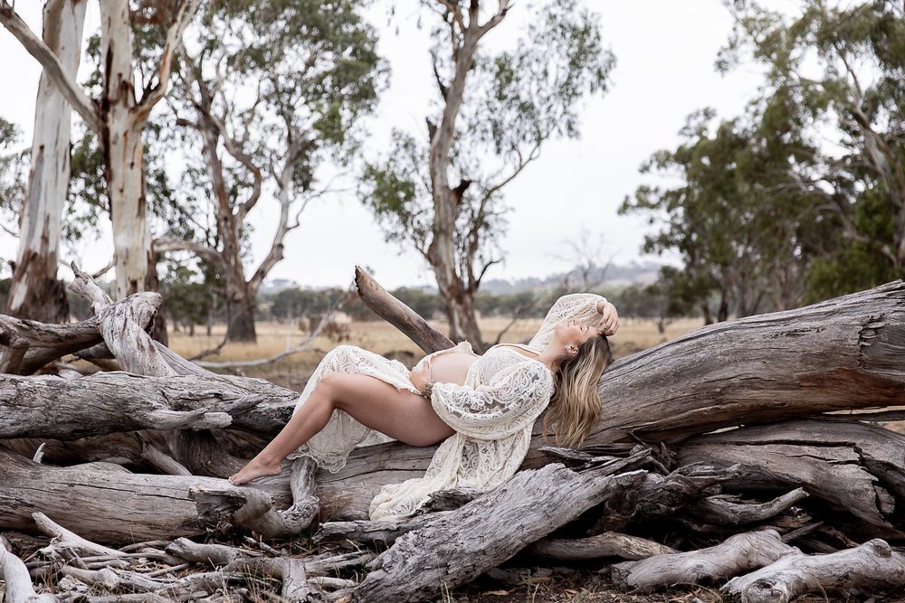 Mother to be laying on a wooden log in the paddock during a professional maternity photo shoot.