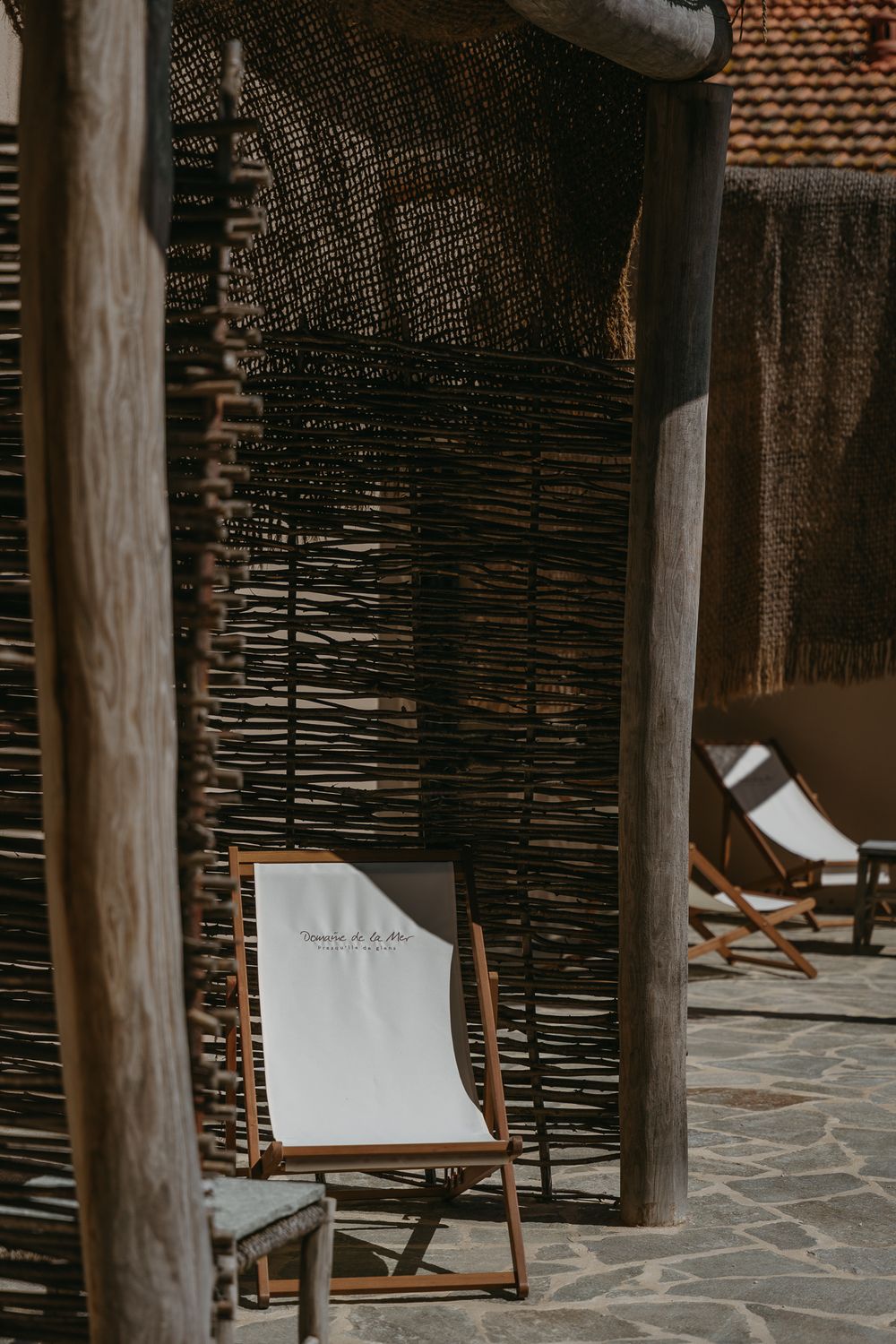Chaises longues en bois avec sièges en tissu blanc disposés sur un patio en pierre près des écrans en bambou tissés dans un complexe.