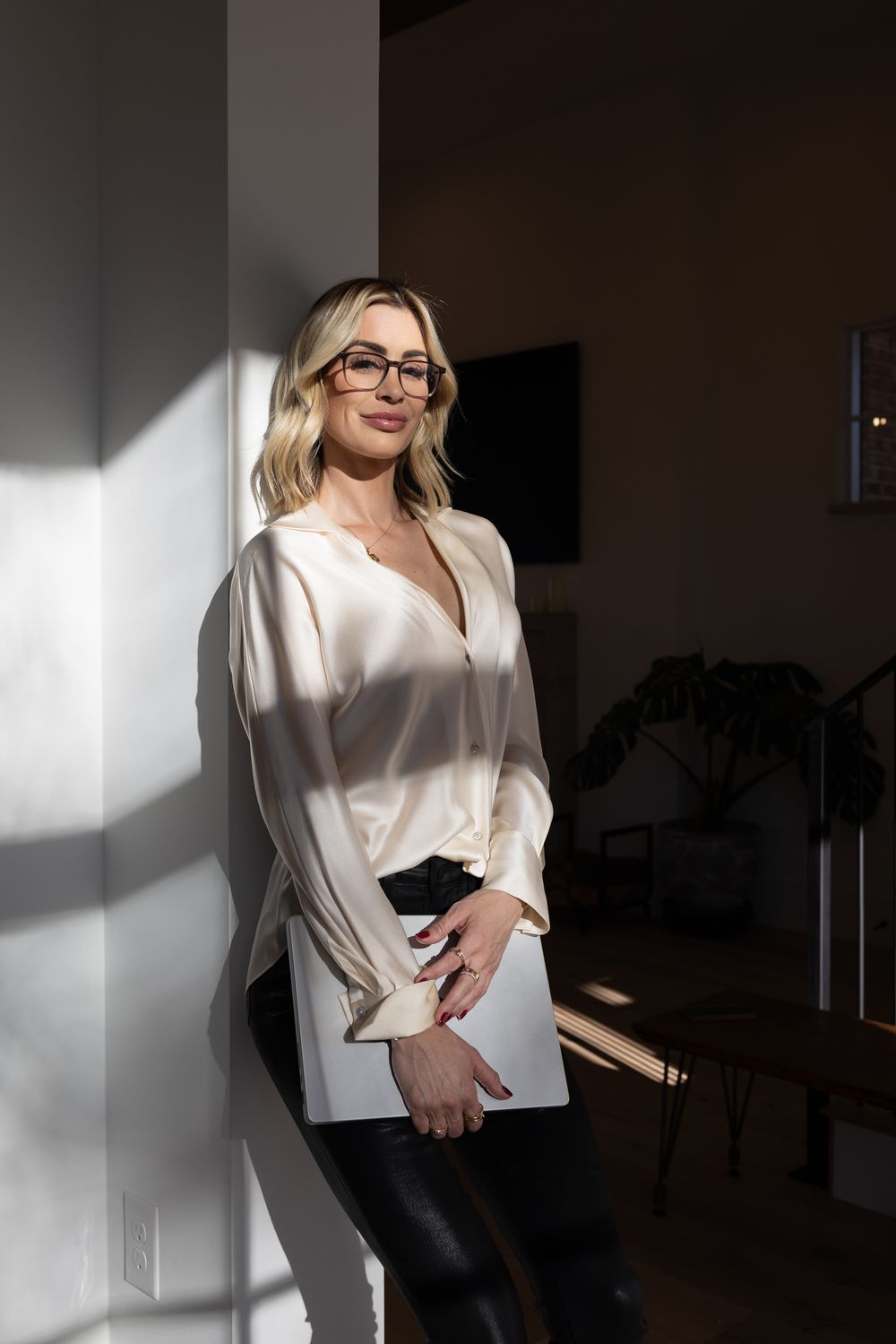 Professional wearing white silk blouse and glasses in dramatic lighting.