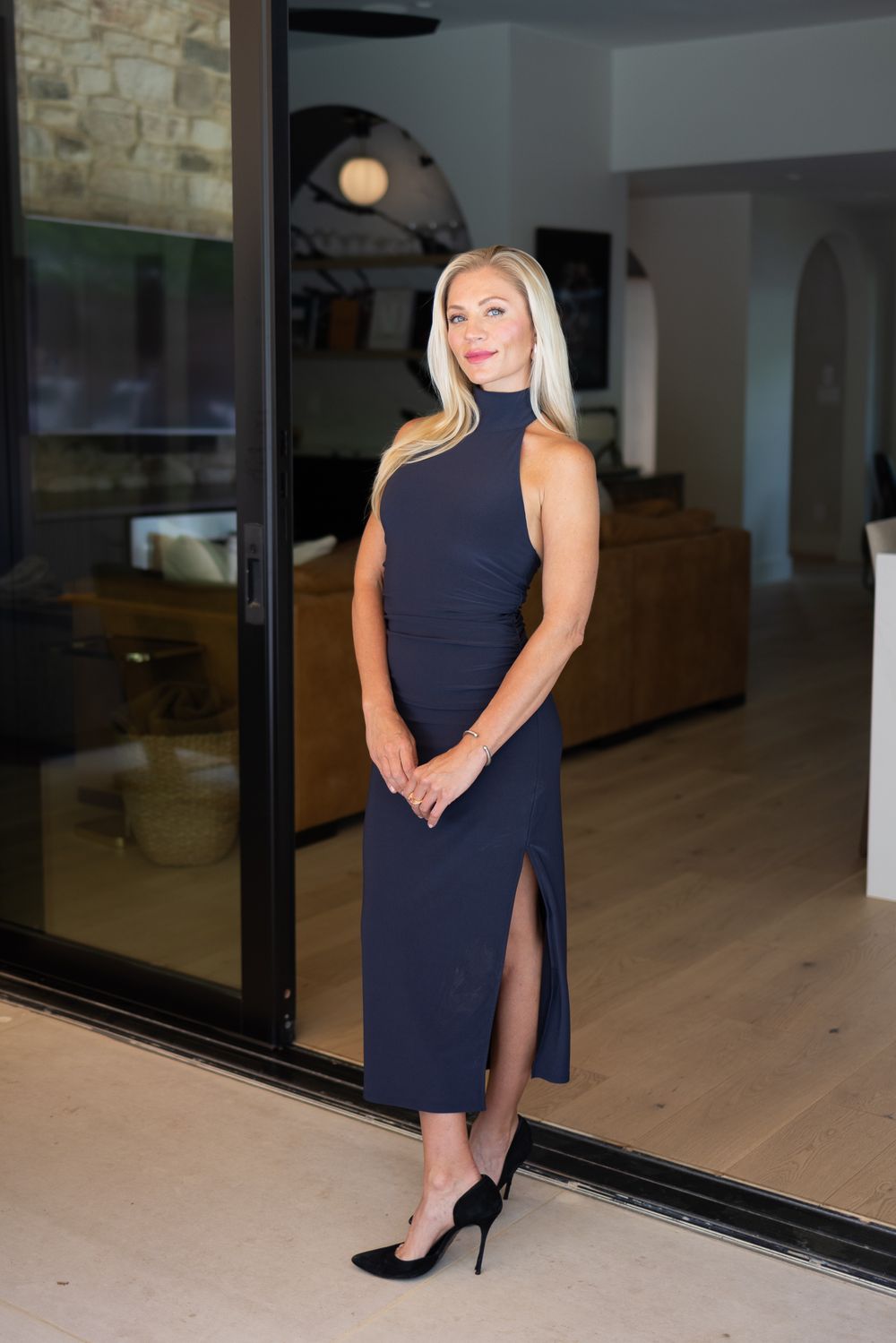 Elegant navy blue sleeveless dress with side slit and black heels in modern interior setting.