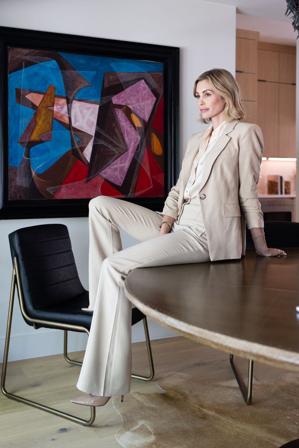 Professional business look featuring cream colored pantsuit against modern art backdrop.
