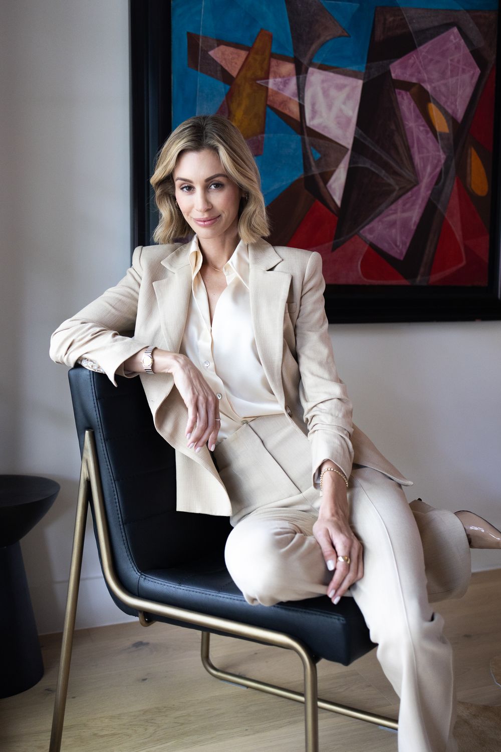 Sophisticated pose in beige business suit with abstract art painting in background.