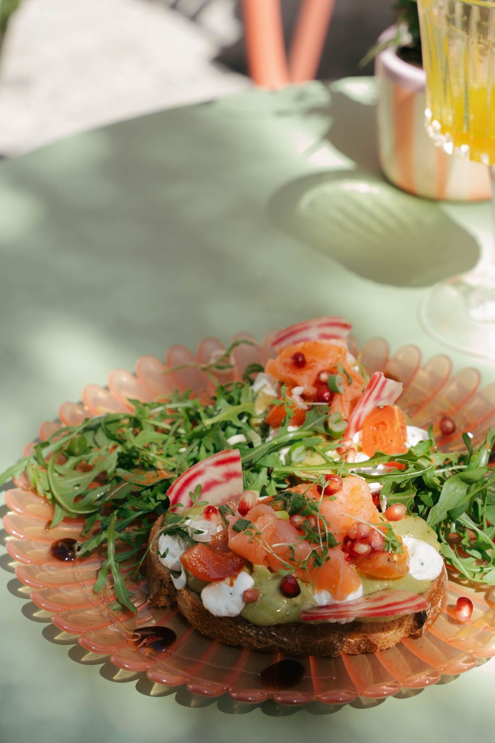 Toast à l'avocat avec saumon fumé, roquette, radis et graines de grenade sur une assiette rose à la lumière du soleil.