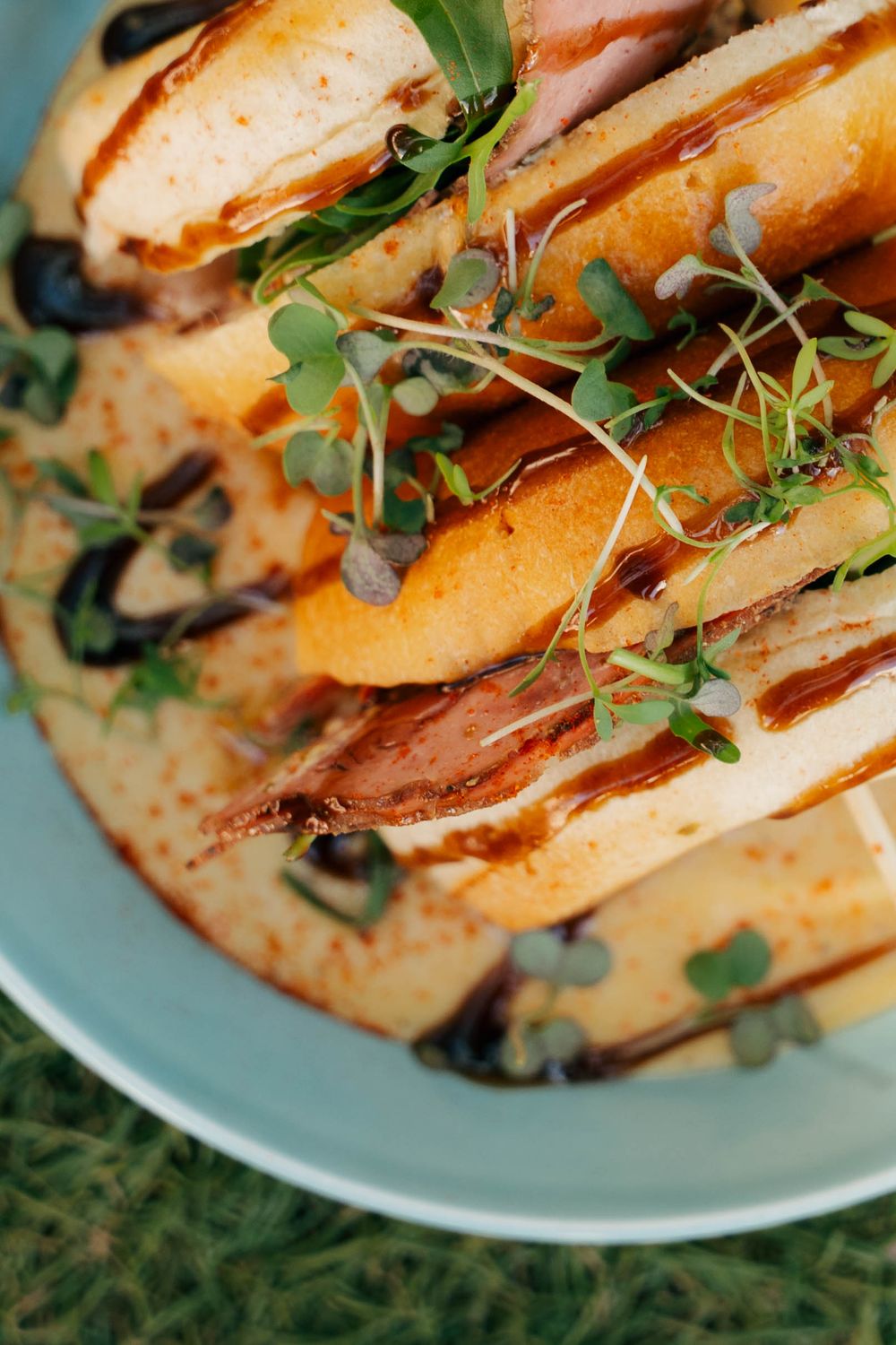 Gourmet open-faced sandwich with ham, melted cheese, microgreens, and balsamic drizzle on a light blue plate.