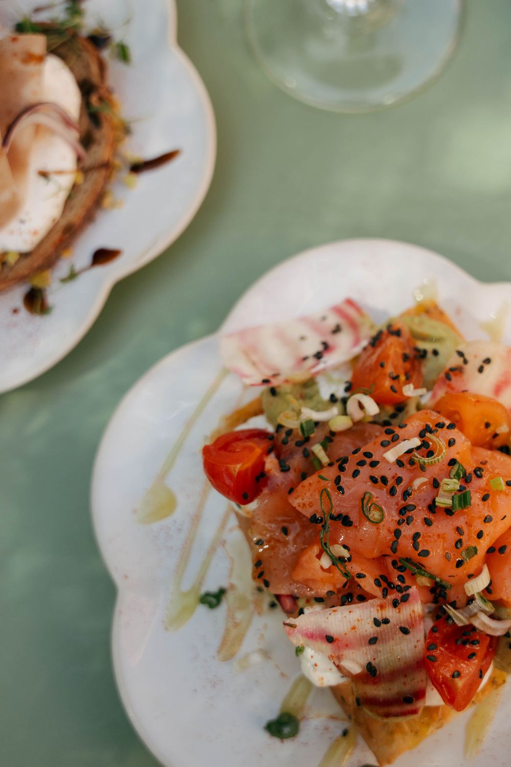 Fresh salmon tartare with black sesame seeds, cherry tomatoes, and herbs served on a white scalloped plate.