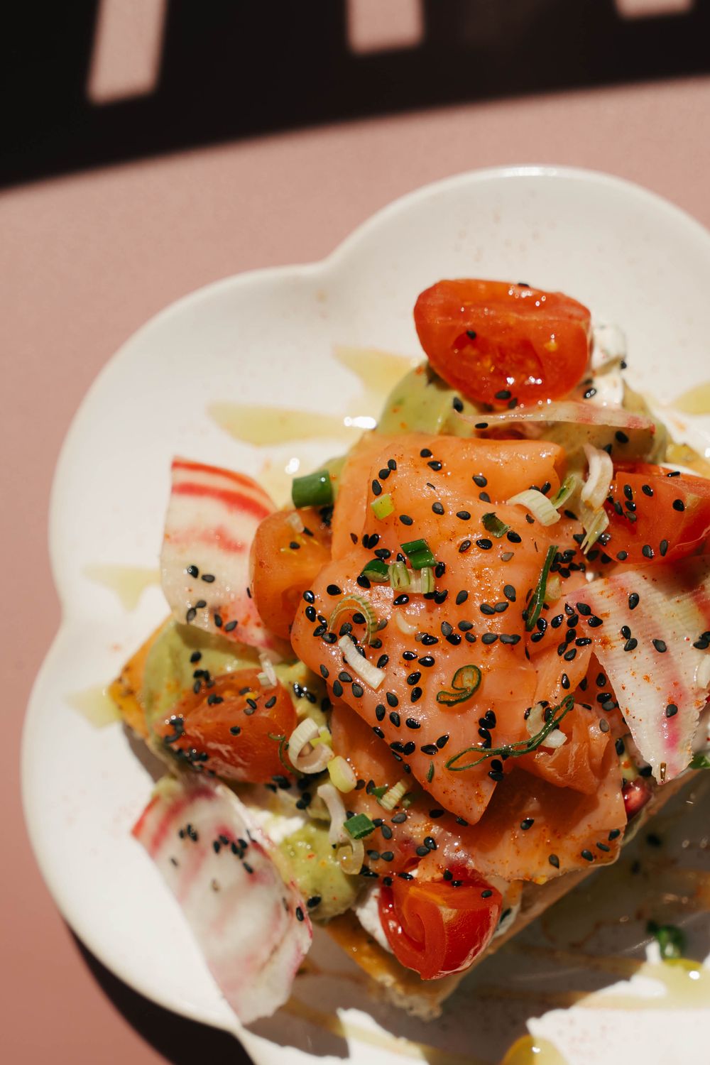 Bol de saumon frais avec tomates cerises, graines de sésame noir, oignons verts et crabe sur une assiette blanche.