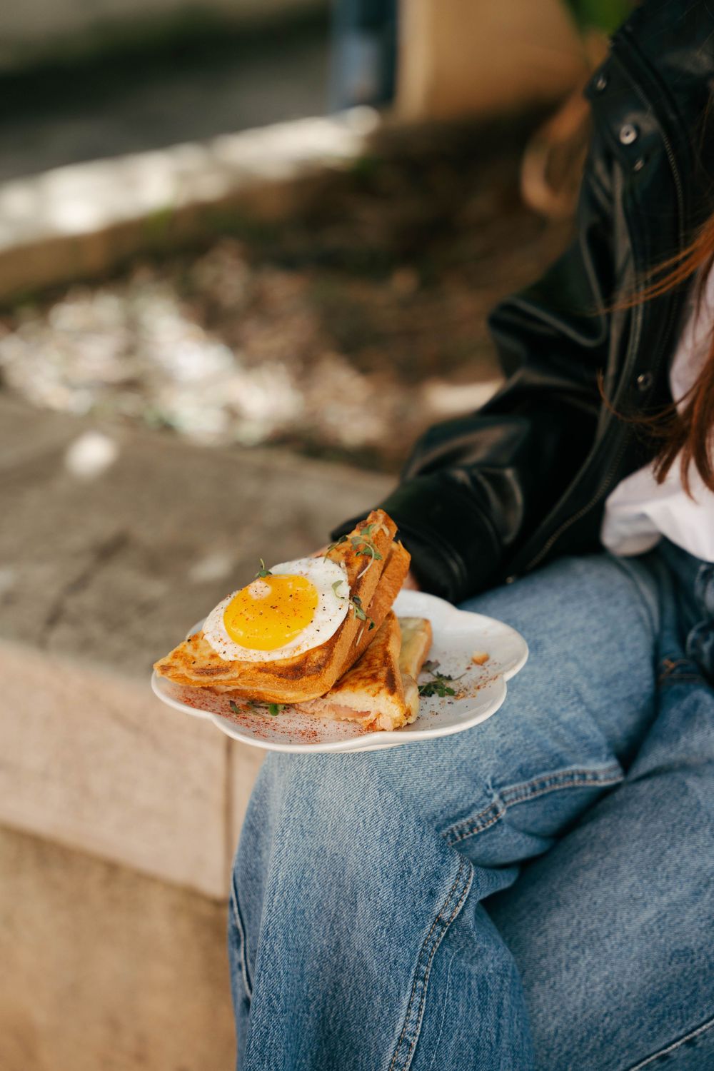 Femme en jean tenant une assiette blanche avec du pain grillé garnie d'un œuf au plat à l'extérieur.