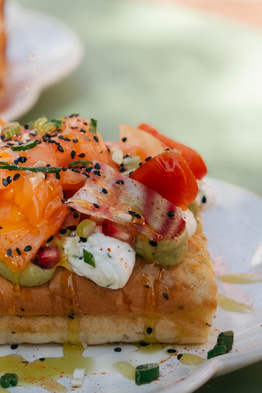 Toast ouvert garni de saumon fumé, de tomates fraîches, de fromage à la crème, d'avocat et de graines de sésame noir sur une assiette blanch