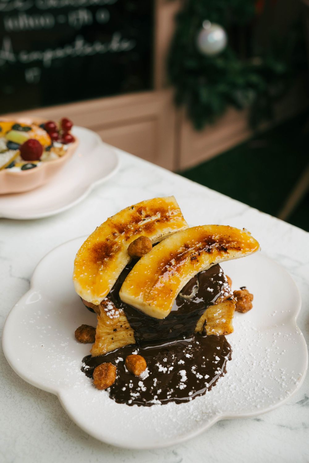 Tranches de banane caramélisées sur sauce au chocolat avec noix et sucre en poudre sur une assiette blanche.
