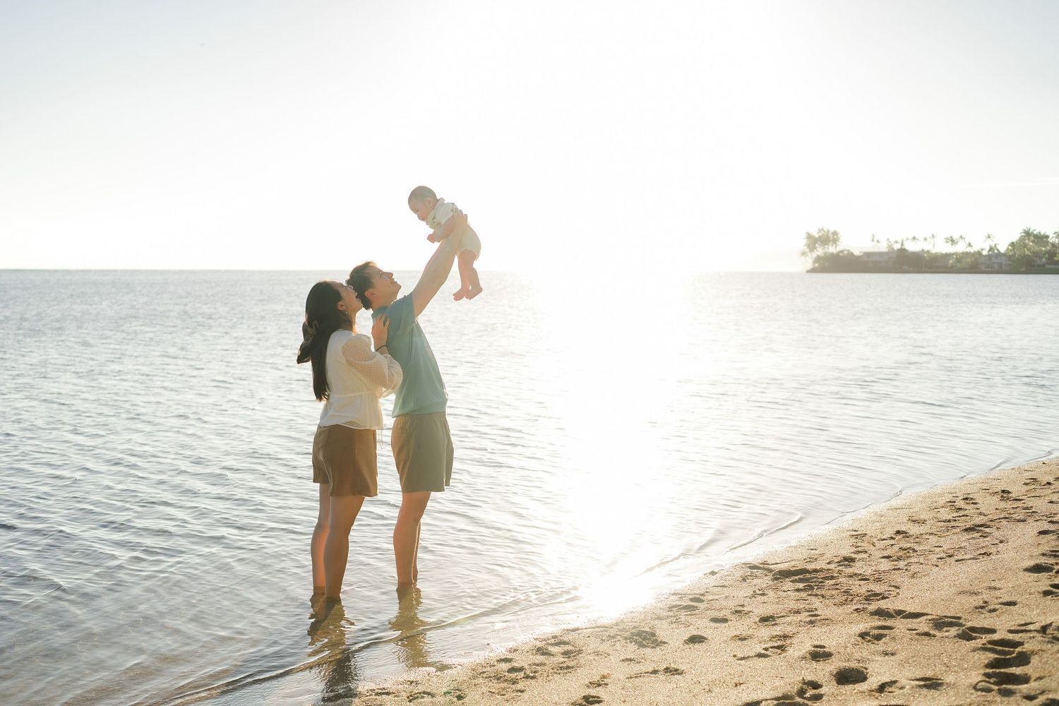 Romantic couple walking along a sandy beach at sunset with sun flare creating a dreamy atmosphere.