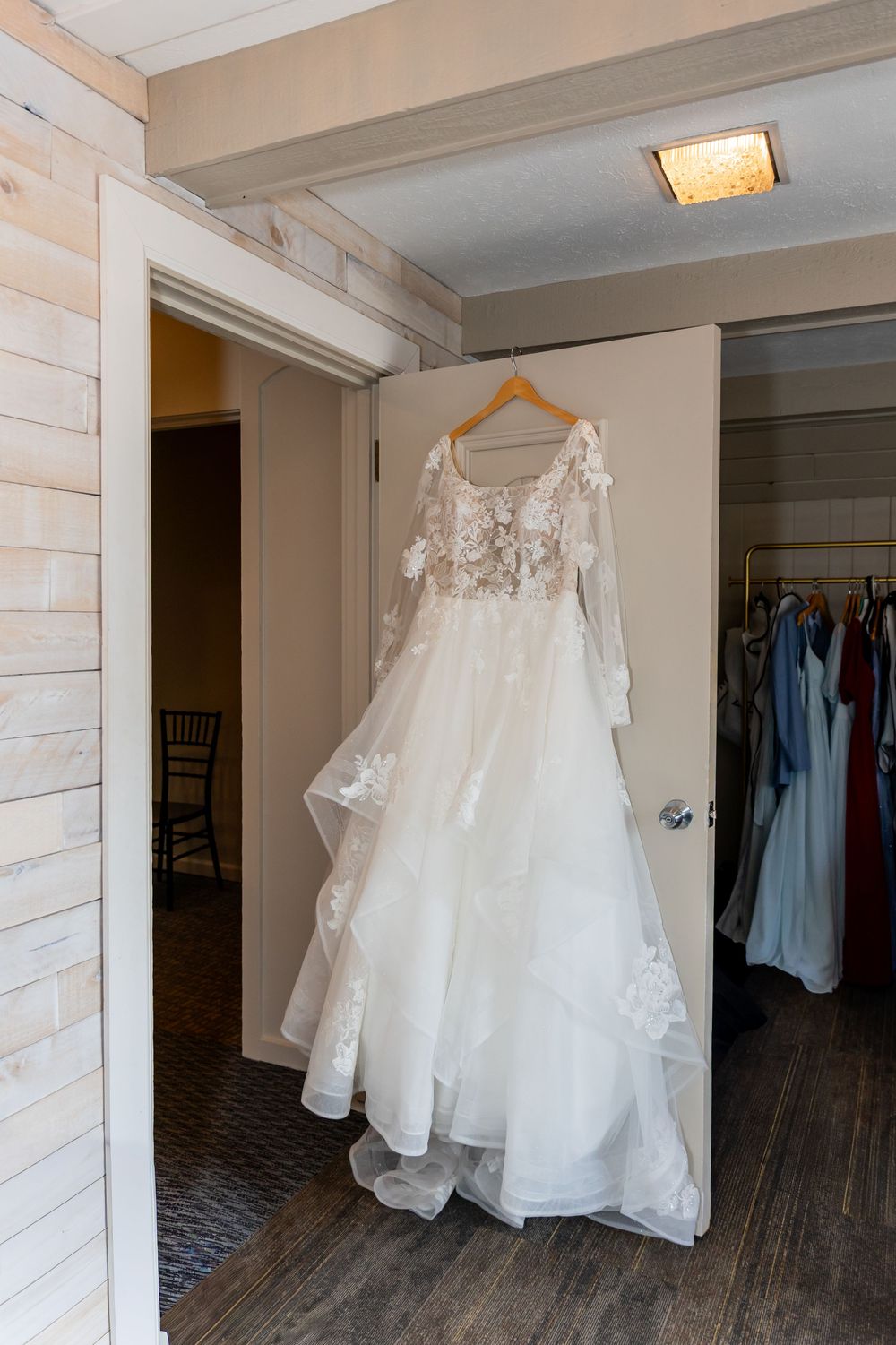 Elegant white lace wedding gown with long sleeves hanging on a wooden hanger in a bridal suite closet.