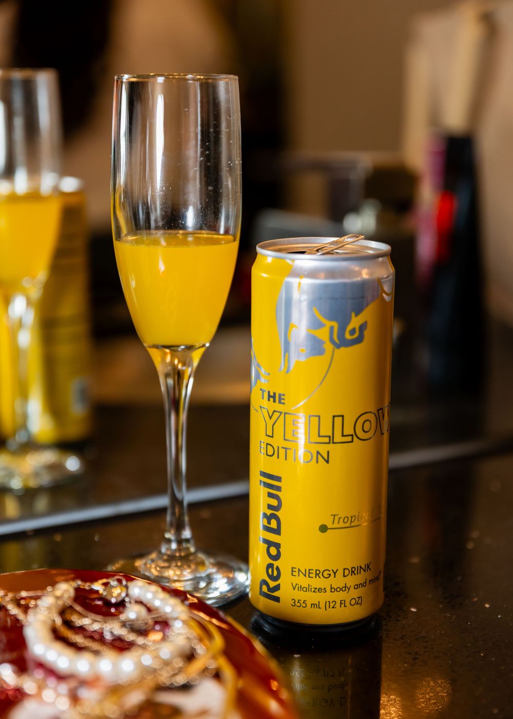 Red Bull Yellow Edition tropical energy drink can beside a champagne flute filled with orange juice mimosa.