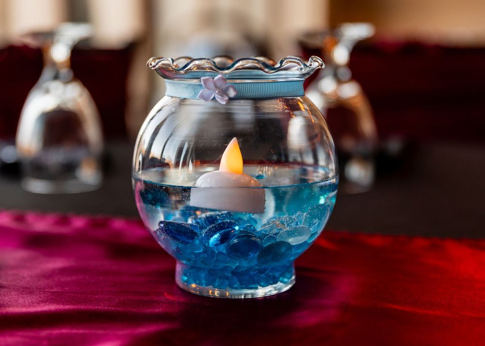 Floating candle in a glass bowl with blue water and gems on a red tablecloth.