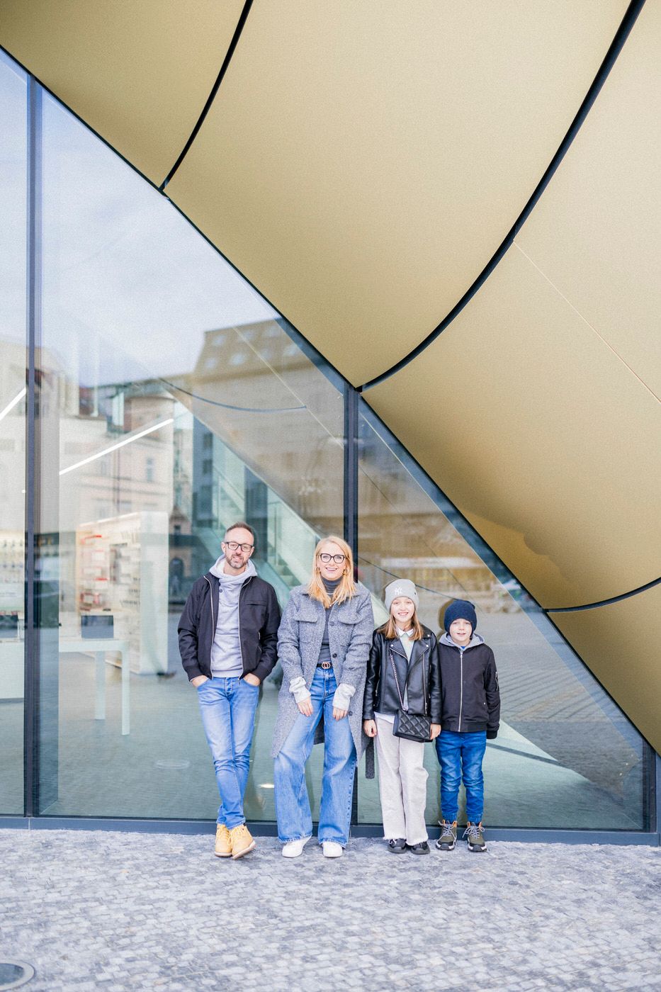 A family of four standing in front of a modern architectural building with glass and curved walls.