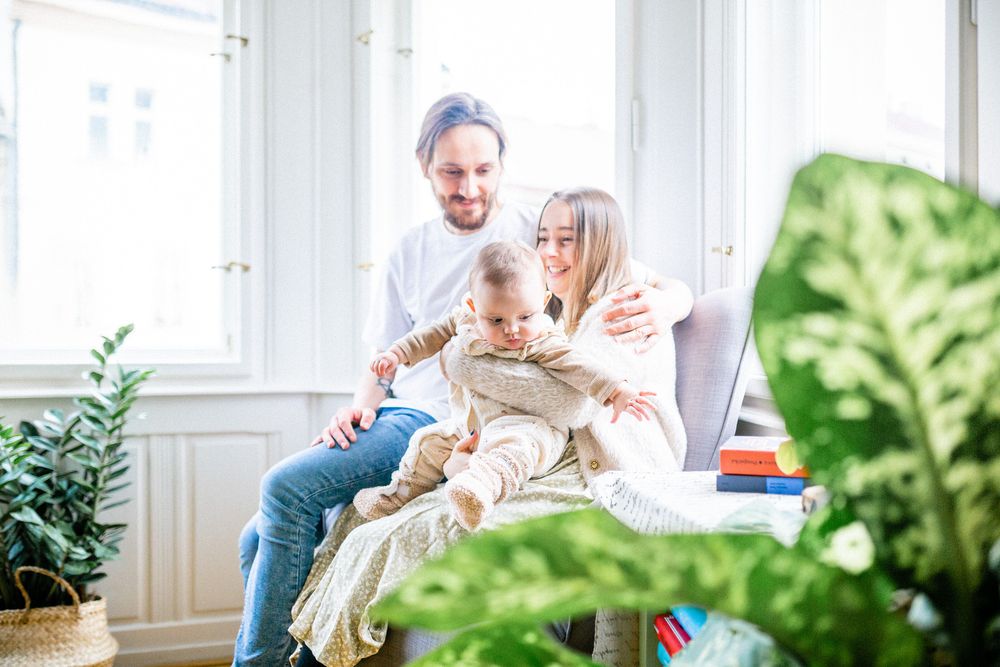 A happy family moment by large windows with indoor plants in the background.