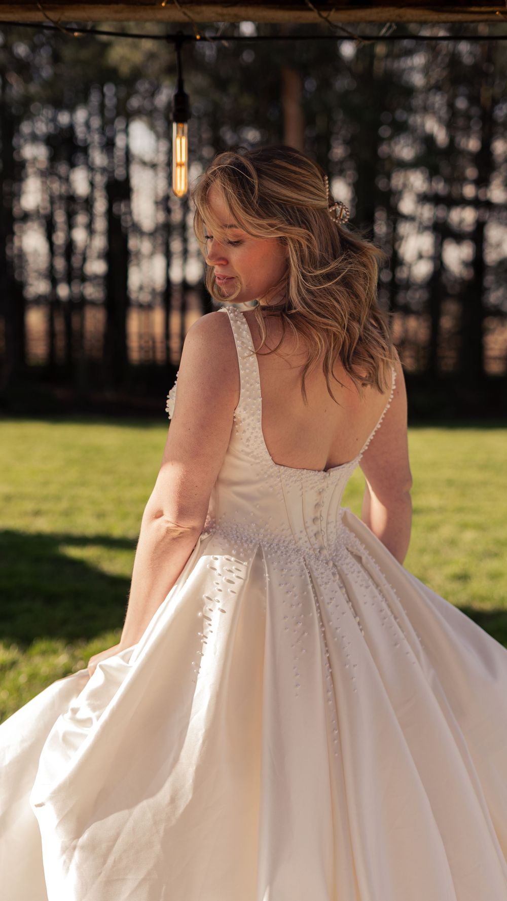 A bride in a stunning backless ball gown wedding dress with floral embellishments twirling outdoors.