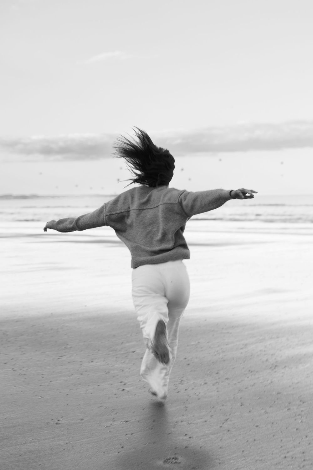 Woman running freely on a beach with arms outstretched and hair blowing in the wind, black and white photo.