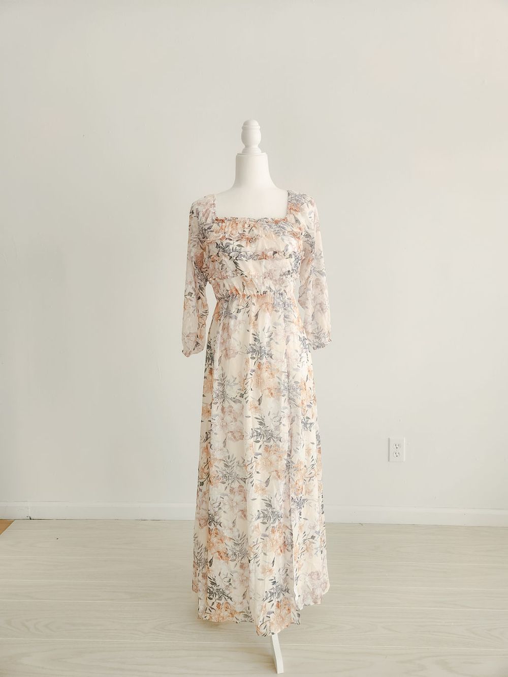 A floral maxi dress with long sleeves and square neckline displayed on a white mannequin against light background.