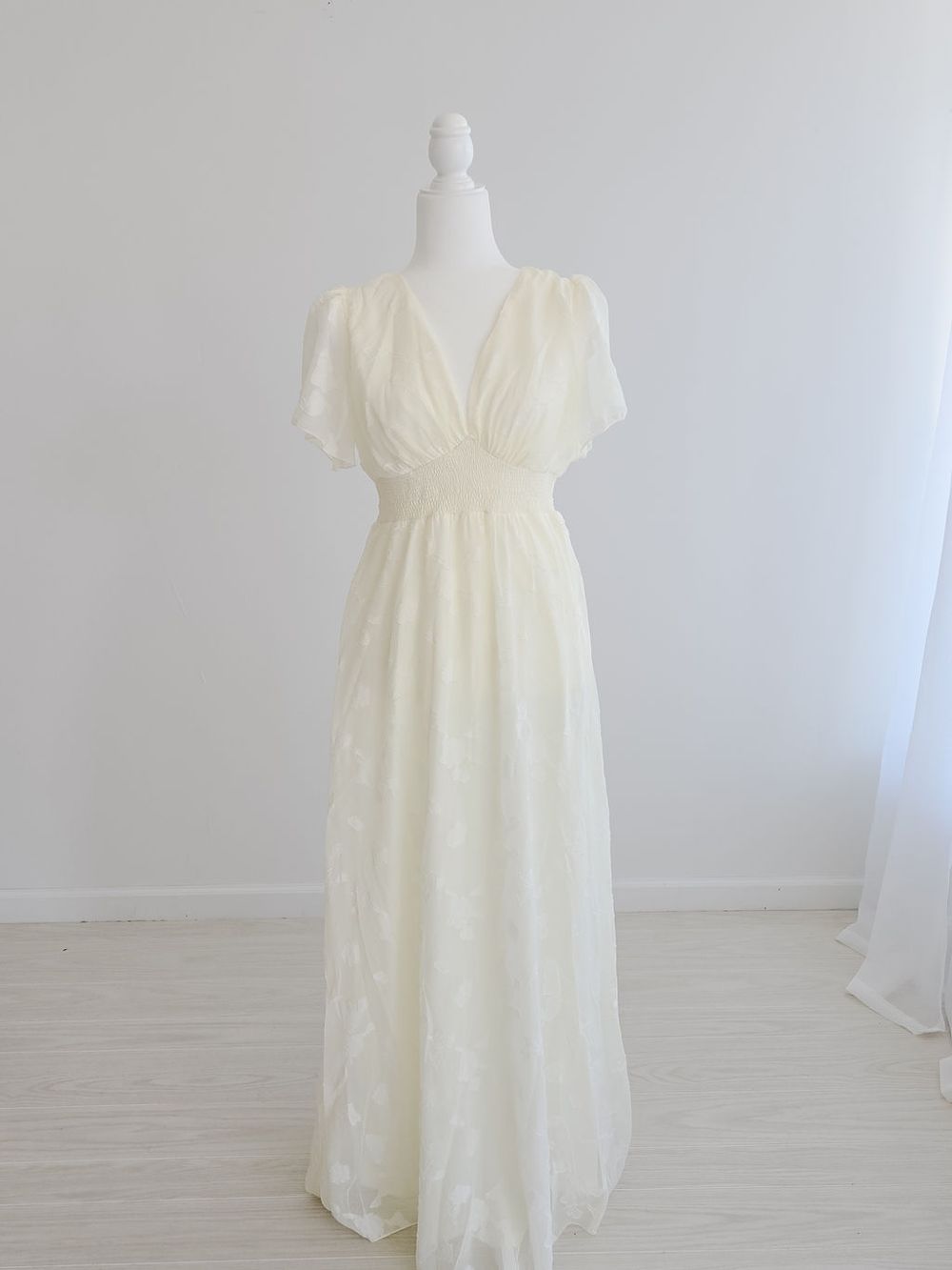 Cream colored empire waist lace maternity dress with short flutter sleeves shown on mannequin from different angles.