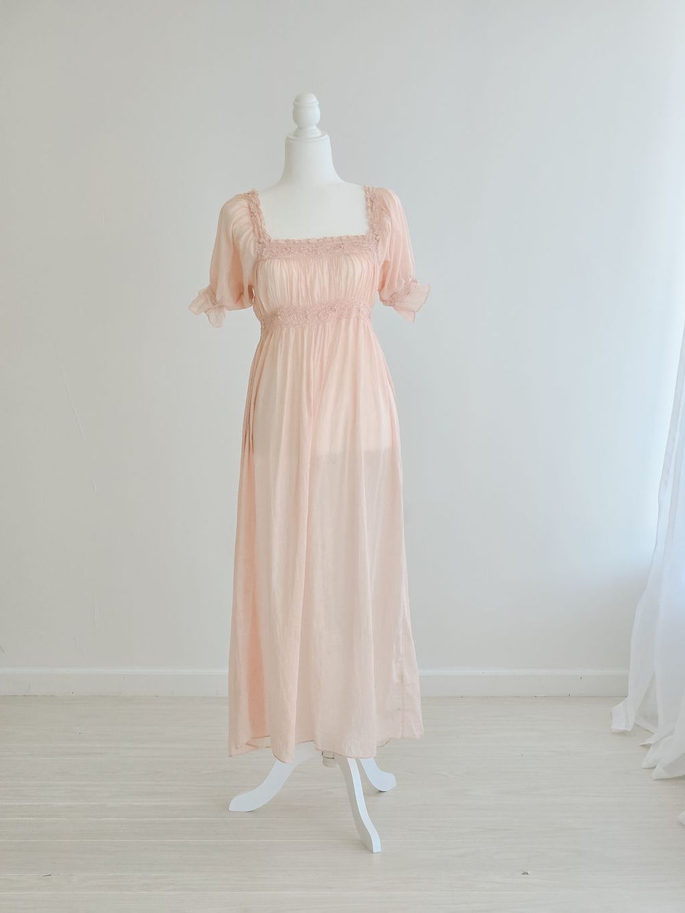 Peach-colored babydoll dress with puff sleeves and square neckline shown on white dress form.