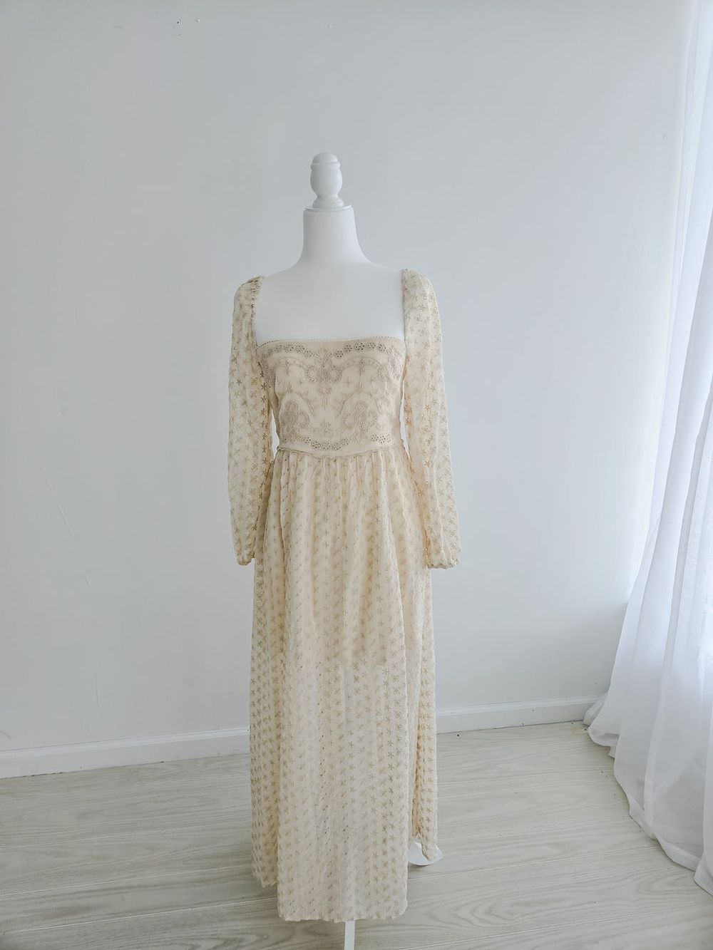 Cream colored vintage-style dress with polka dots and long sleeves shown on dress form.