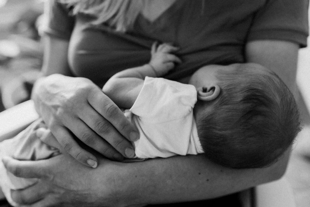 Vastasyntynyt vauva äidin rintaa vasten perheen kotona postpartum- ja vauvakuvauksessa.