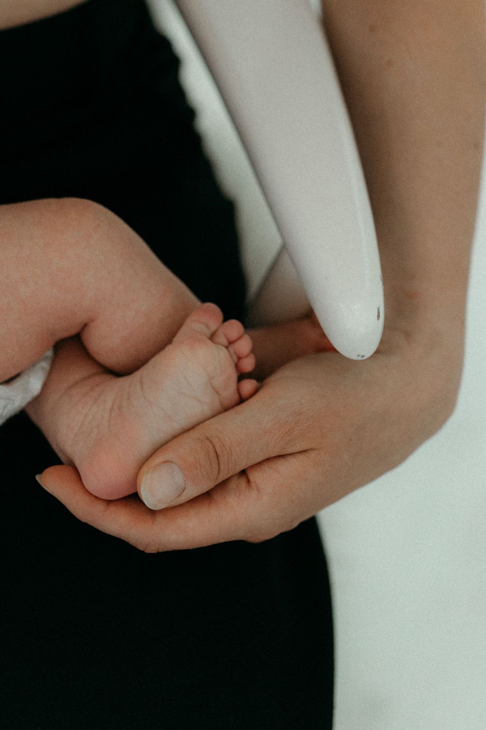 Lähikuva vastasyntyneen vauvan jalkapohjasta äidin kättä vasten kotona postpartum- ja vauvakuvauksessa.