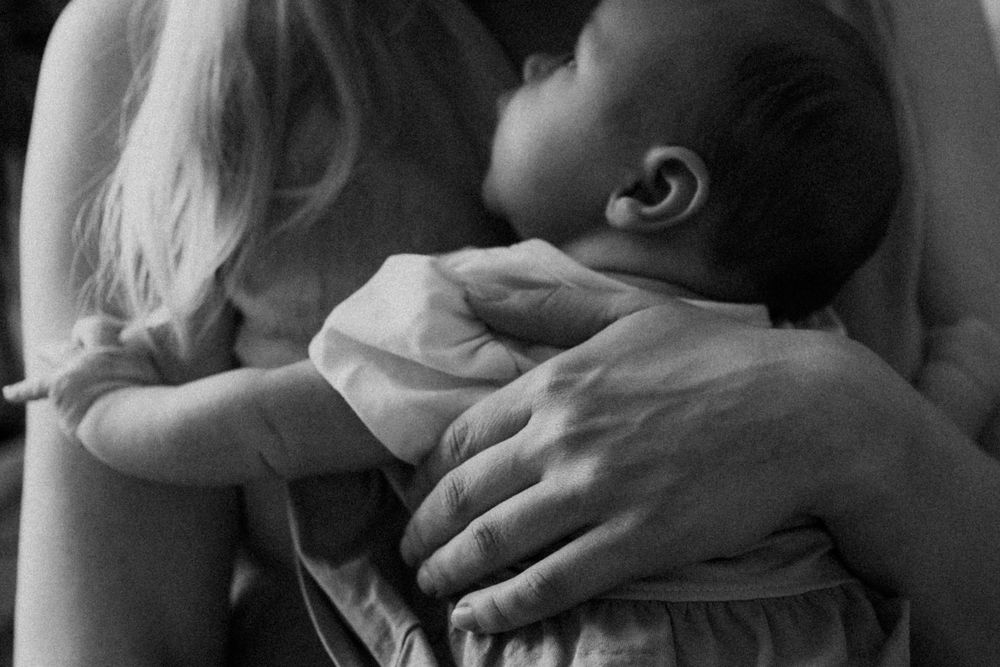 Vastasyntynyt vauva äidin rintaa vasten perheen kotona postpartum- ja vauvakuvauksessa.
