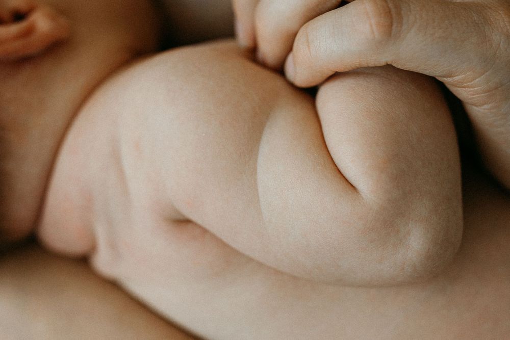 Lähikuva vastasyntyneen vauvan niska- ja selkäpoimuista perheen kotona postpartum- ja vauvakuvauksessa. Äiti pitää kädestä kiinni.Imetyskuva