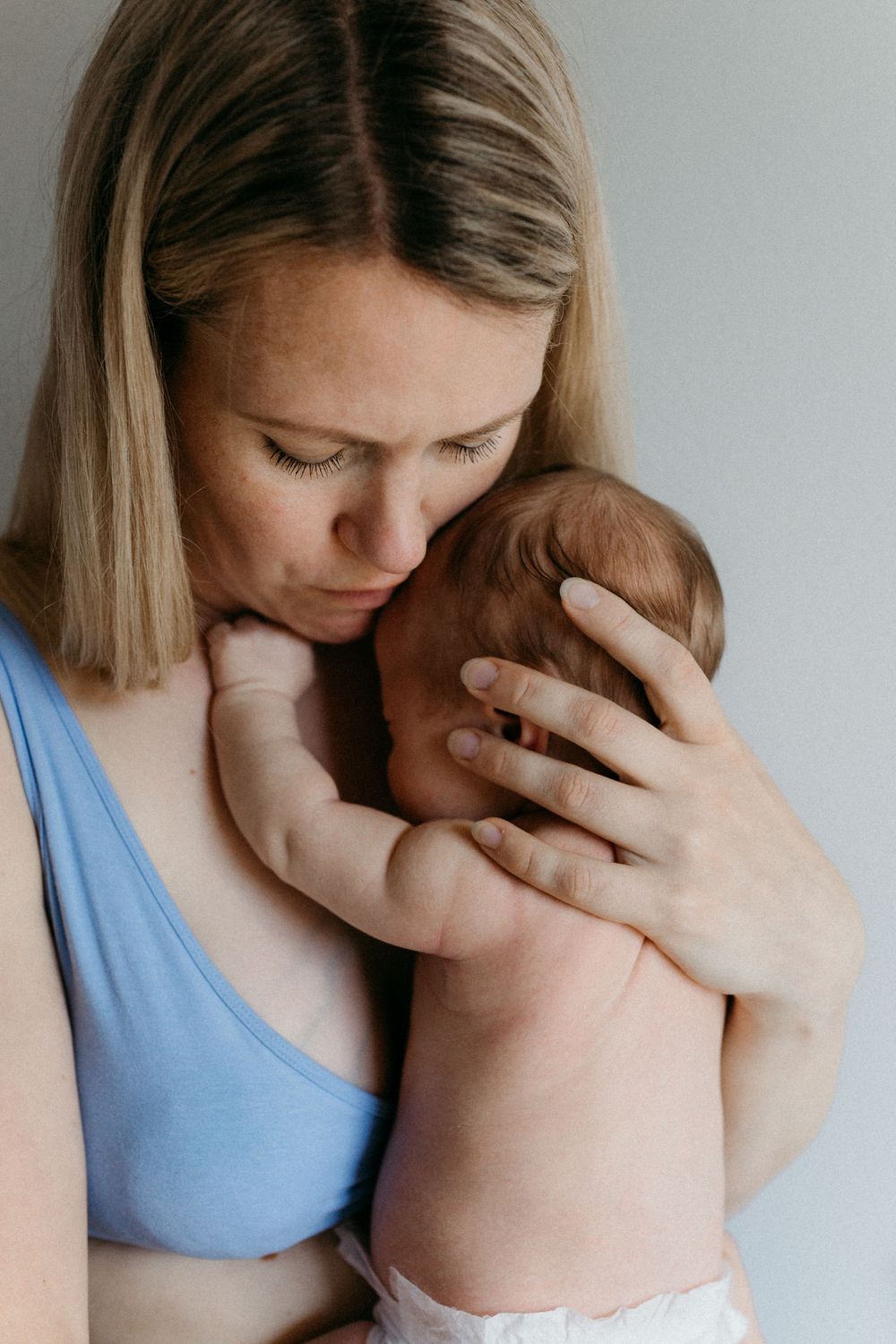 Vastasyntynyt vauva äidin rintaa vasten turvallisesti perheen kotona postpartum- ja vauvakuvauksessa. Äidillä rauhoitteleva ilme.