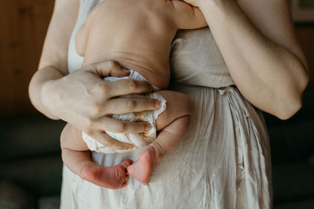 Lähikuva, jossa vastasyntynyt nukkuu äidin rintaa vasten vaippasiltaan perheen kotona postpartum- ja vauvakuvauksessa.