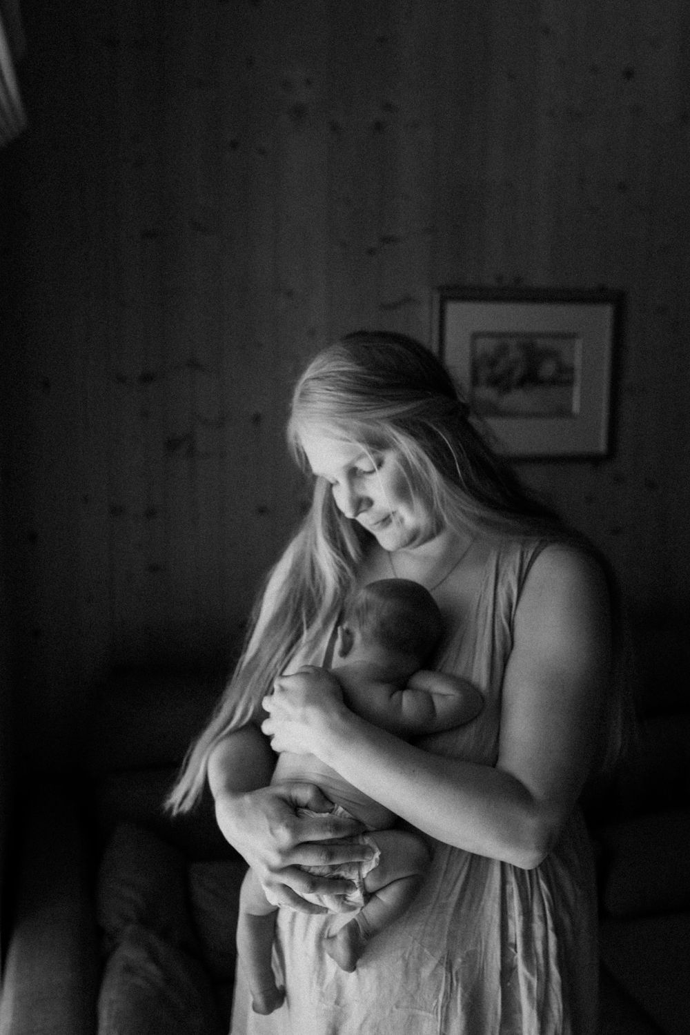 Vastasyntynyt vauva nukkuu äidin rintaa vasten vaippasiltaan perheen kotona postpartum- ja vauvakuvauksessa.