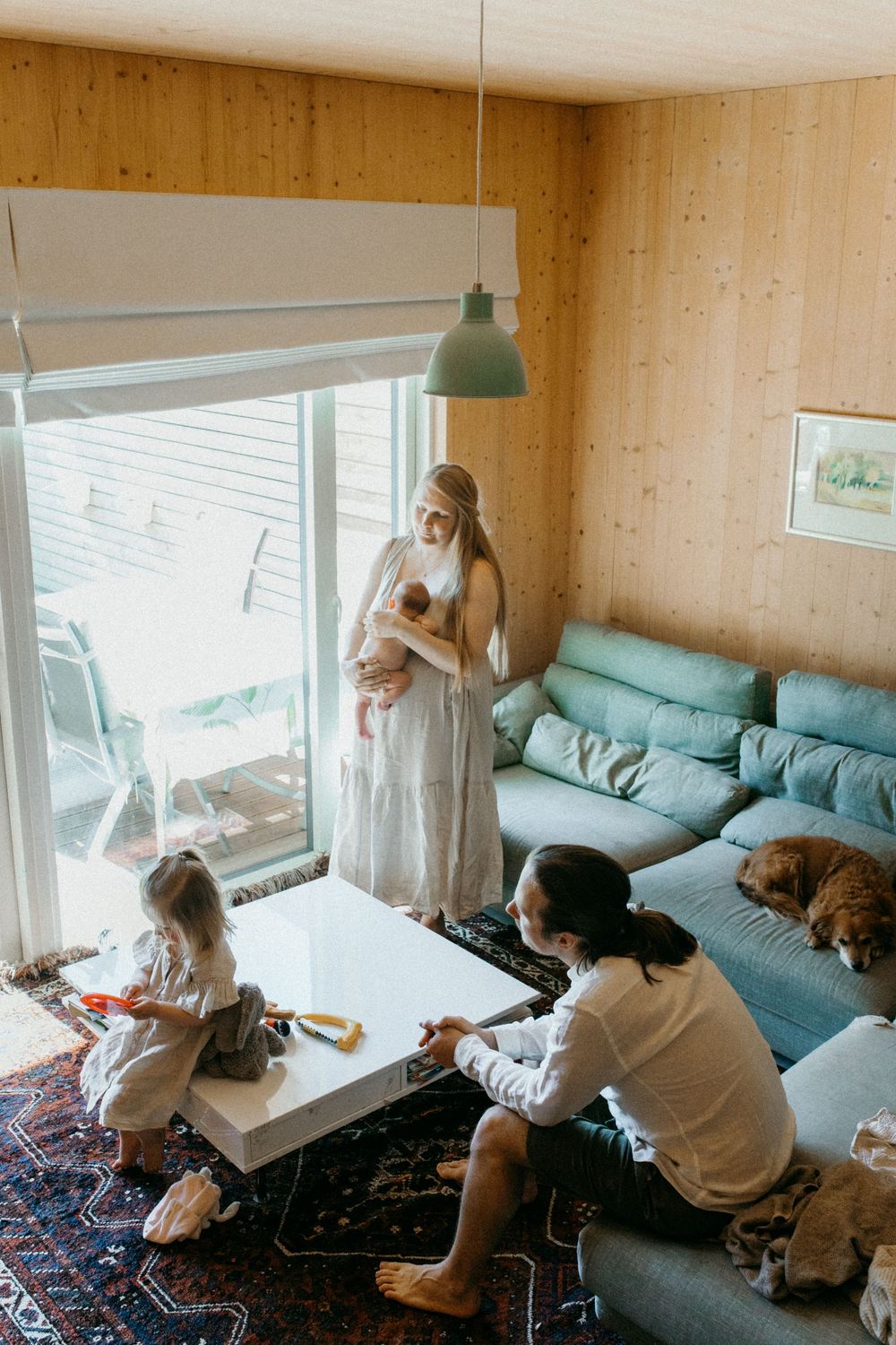 Perhe viettää yhteistä aikaa Vastasyntynyt nukkuu äidin sylissä perheen kotona postpartum- ja vauvakuvauksessa. Isosisko esittelee lelujaan.