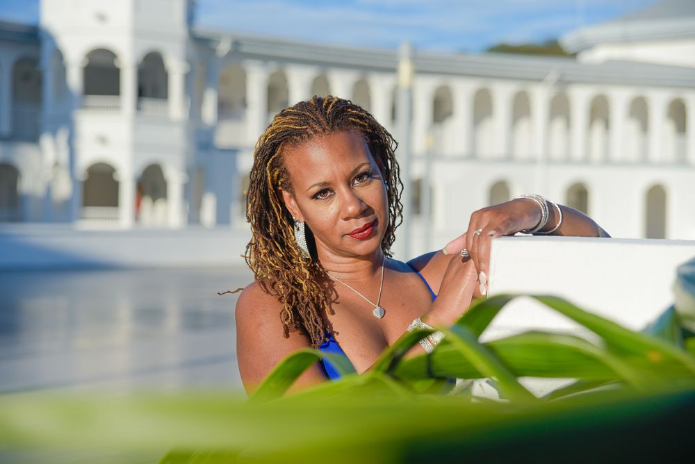 Outdoor photoshoot with person in blue dress against white colonial architecture and blue sky.