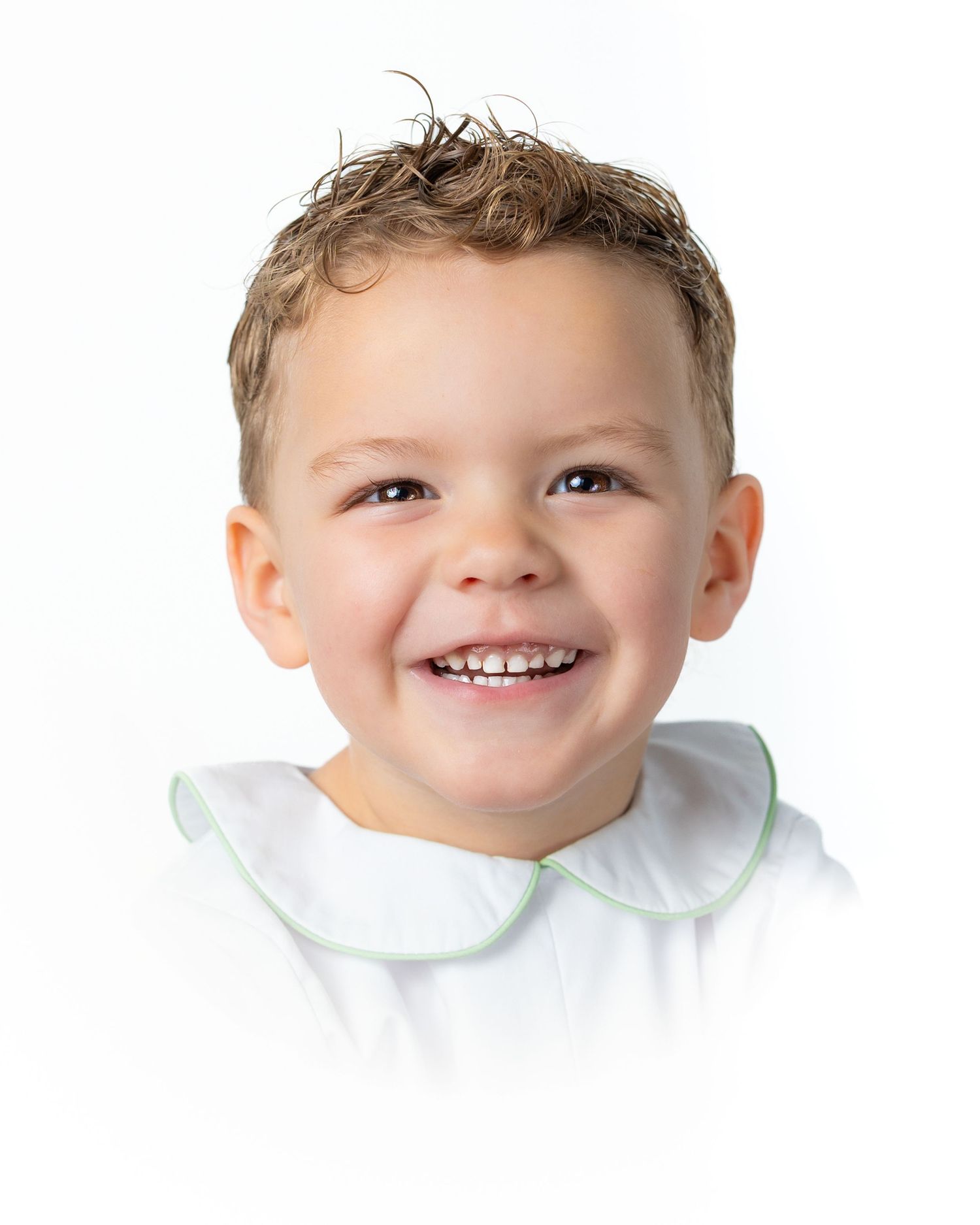 Portrait of a young child wearing a white smocked dress and white bow against a white background.