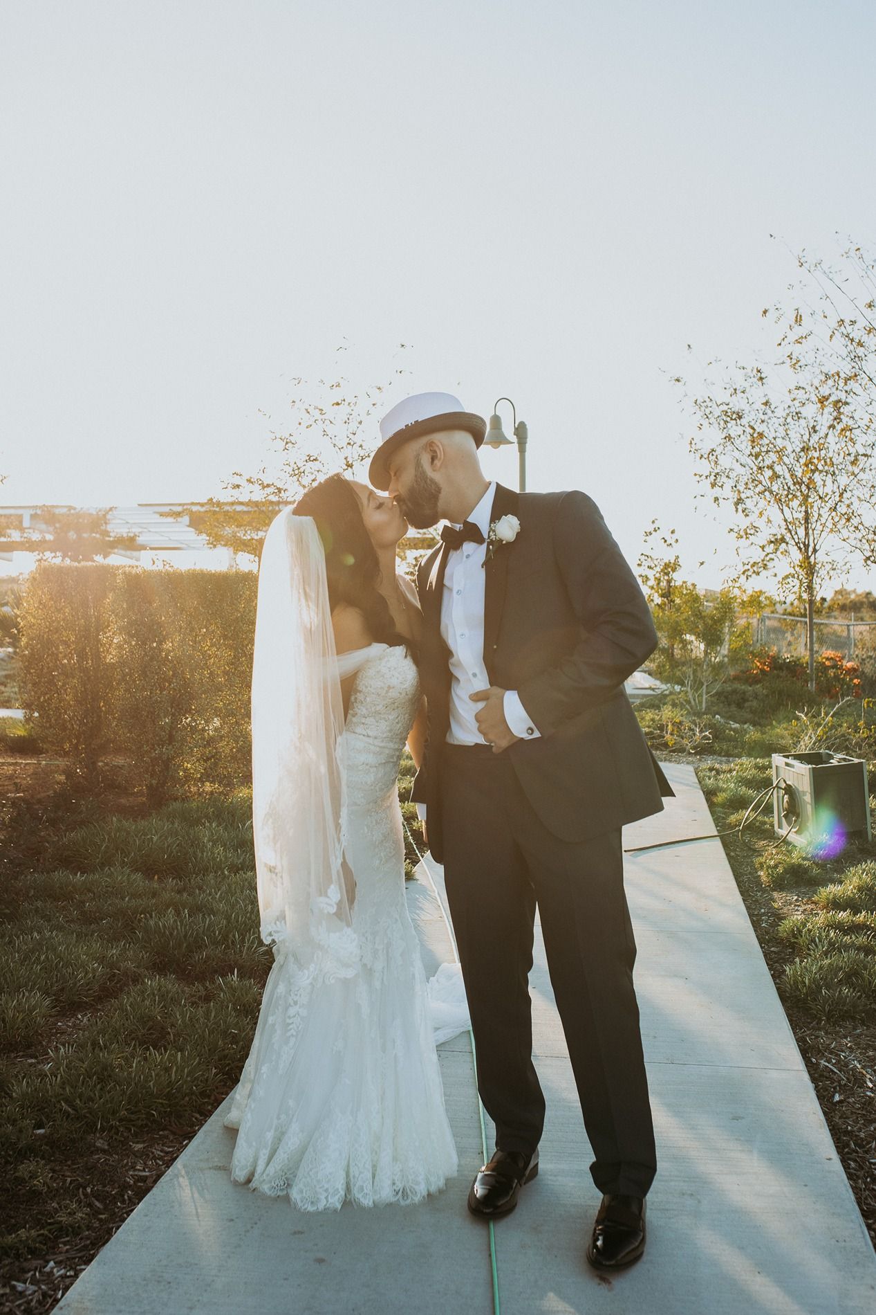 A romantic wedding couple embraces during sunset on a pathway with golden sunlight streaming through the trees.