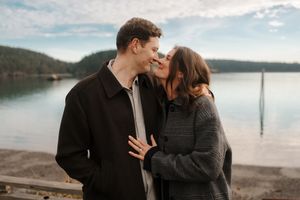Romantic couple sharing intimate moments by a serene lakeside during sunset with mountains in the background.